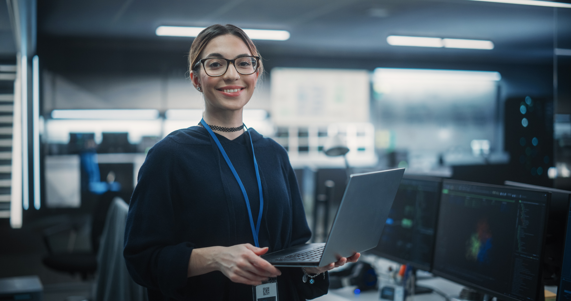 a portrait of a woman holding a laptop confidently while monitoring technology