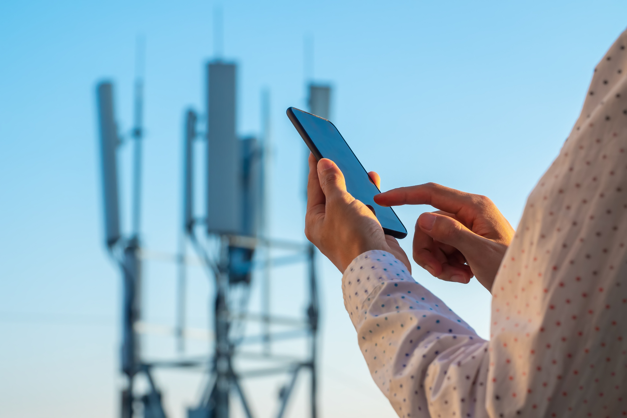 a photo of someone using a smart phone with a cell tower in the background